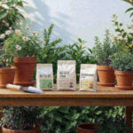 Three bags of fertilizer lined up on a potting bench with a hand trowel